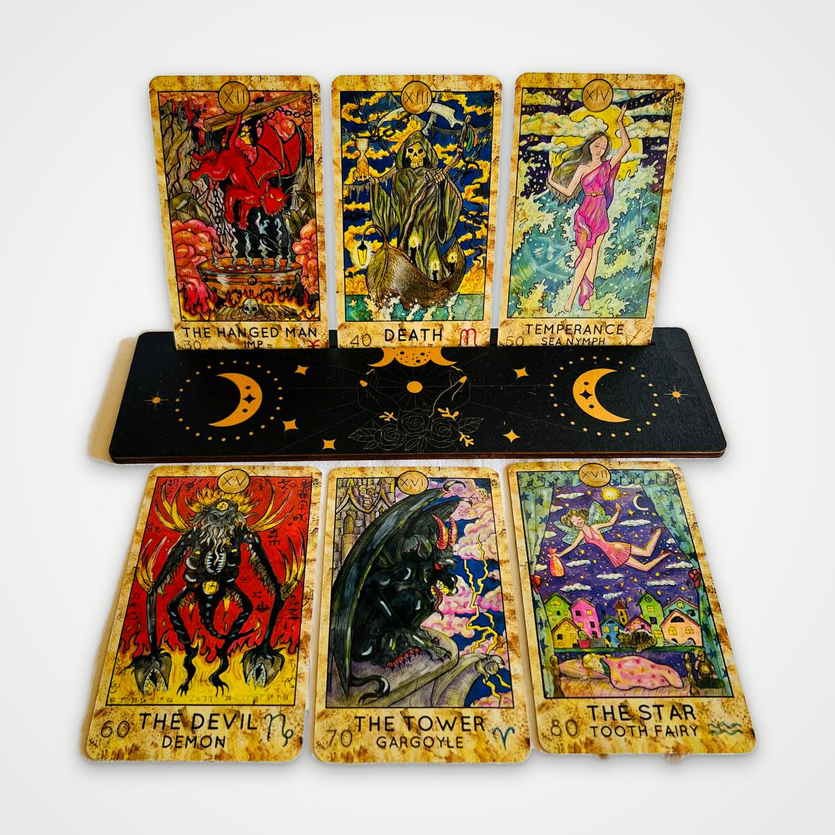 Fantasy World Tarot cards on a wooden stand: The Hanged Man, Death, Temperance, The Devil, The Tower, The Star