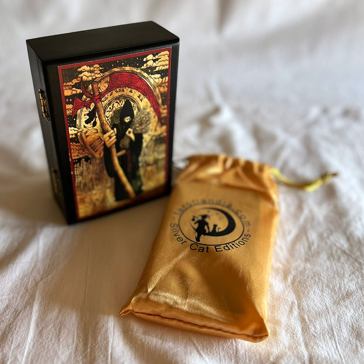 Black wooden box standing next to the golden satin pouch with the Silver Cat Editions logo